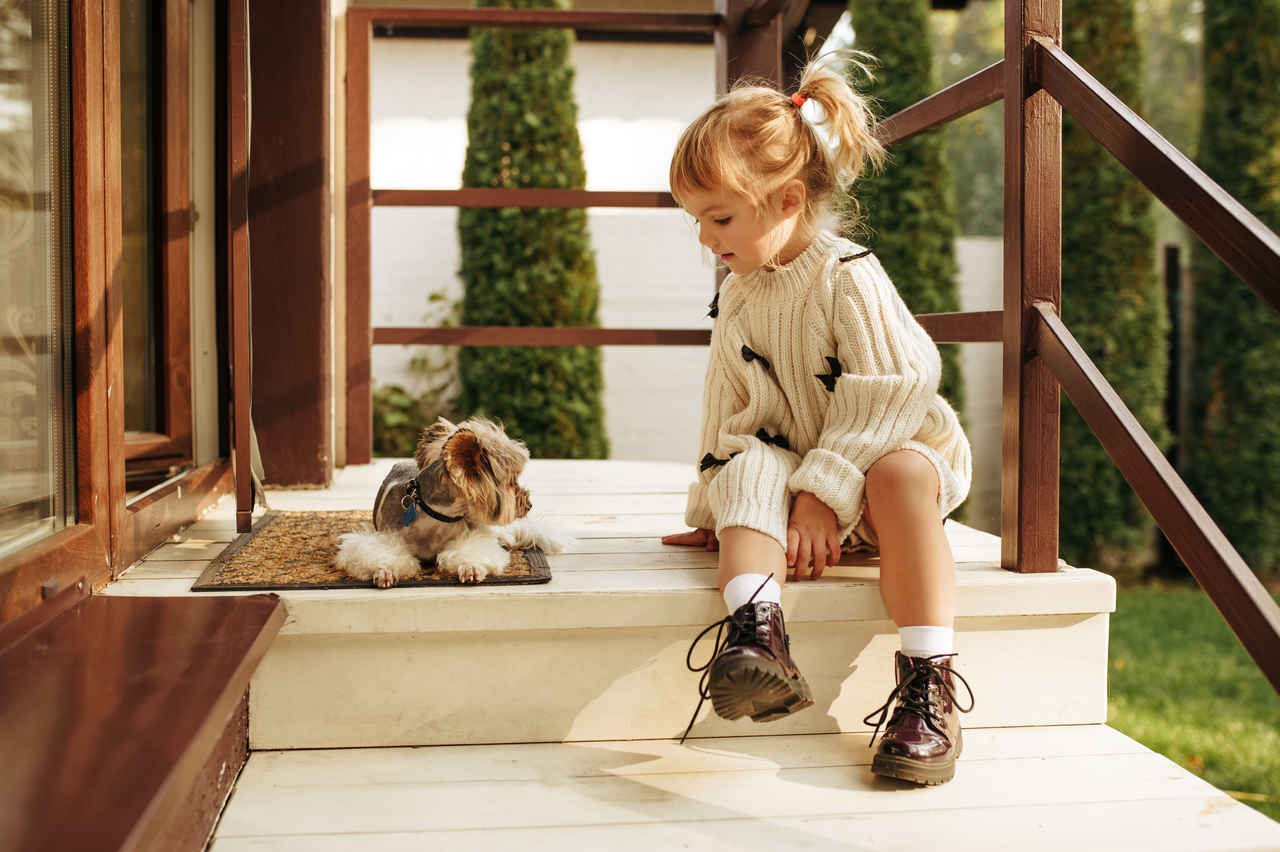 evin kapısının girişinde oturan küçük bir kız ve küçük köpek